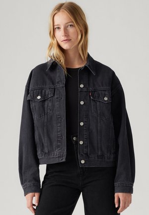 Black denim jacket with a collar, front pockets, and silver hardware. Loose fit with long sleeves and a cropped design. Textured fabric.