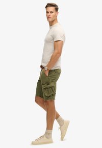 Beige cotton t-shirt, olive green cargo shorts with side pockets, beige sneakers, and knit socks. Simple design with functional elements.