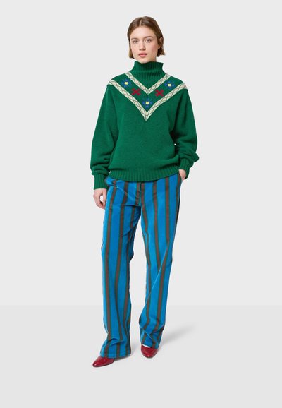 Zelena pletena rolka s cvjetnim vezom, u paru s plavim i smeškim prugastim hlačama i crvenim potpeticama.