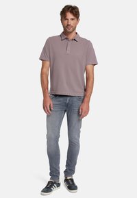 Korte mouwen, geknoopte polo in licht mauve, gecombineerd met lichtblauwe slim-fit jeans en donkerblauwe sneakers met witte accenten.