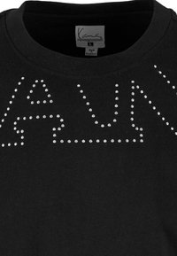 Melnas kokvilnas T-krekls ar apaļu kaklu un rhinestone rotājumiem, kas veido burtus uz priekšpuses. Skaņas birka redzama kakla apgabalā.