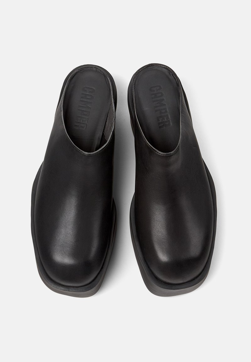 Mules de cuero negro con parte trasera abierta, punta redondeada y diseño minimalista con textura suave y suela de goma en contraste.