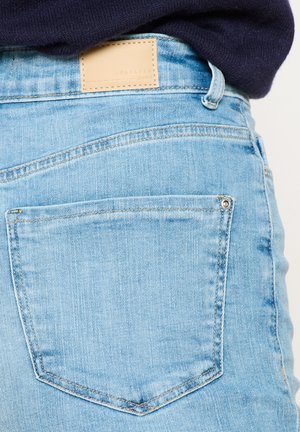 Heledad sinine teksapüksid, millel on kolmnurkse kujuga tagatasku, nahast silt vöökohtadel ja õrn õmblusdetail.