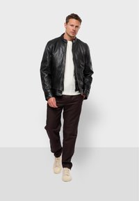 Black leather jacket with a minimalistic design, standing collar, and zip closure, paired with a white shirt and dark pants. Light sneakers.