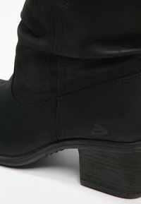 Botín negro de tobillo hecho de cuero suave, con un tacón bajo y detalles de costura sutiles. El diseño incluye un logotipo en el lateral.