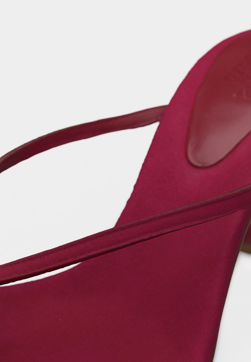 Gros plan d'une chaussure slingback rouge profond avec des lanières fines et une matière supérieure lisse sur fond blanc.