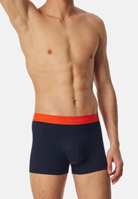 Boxer shorts in cotone blu con elastico arancione in contrasto, caratterizzato da testo in rilievo. Elastica in vita per comfort e vestibilità, lunghezza fino a metà coscia.