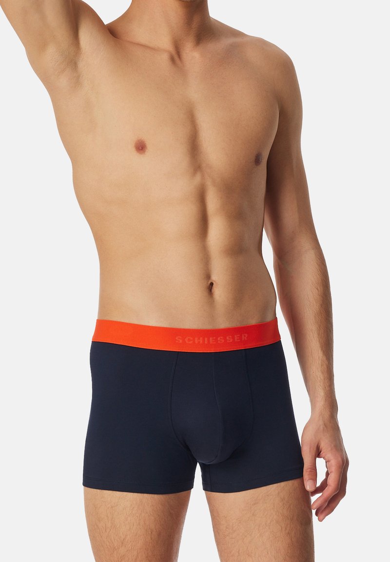Boxer shorts in cotone blu con elastico arancione in contrasto, caratterizzato da testo in rilievo. Elastica in vita per comfort e vestibilità, lunghezza fino a metà coscia.