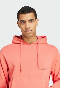 Koraal hoodie met een voorzak, capuchon met trekkoord en een reliëf logo "Fussballliebe Adidas Football". Zachte katoenmix textuur.