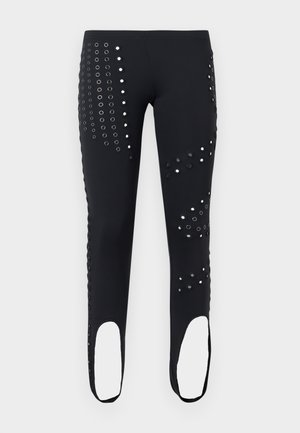 Fekete leggings ezüst függesztékes mintákkal és kengurukapcsokkal a bokáknál, egyszínű világosszürke háttéren bemutatva.