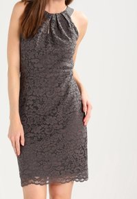 Robe en dentelle grise avec une silhouette ajustée, présentant un corsage plissé, un décolleté en goutte d'eau et un ourlet festonné. Tissu lisse accentué aux épaules.
