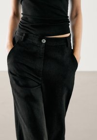 Zwarte linnen broek met een aangesloten tailleband, knoopsluiting aan de voorkant en zijzakken. Heeft een ontspannen pasvorm en een soepele textuur.