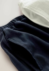 Tumed kangast püksid elastse vöökohtaga ja küljetaskutega, koos volditud valge tipuga. Sile tekstuur, igapäevane disain.