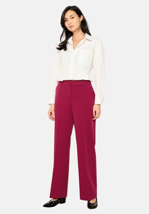 White button-up shirt with a chest pocket, paired with high-waisted, wide-leg burgundy trousers and black shoes with circular accents.