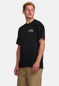 Black cotton t-shirt with short sleeves, featuring a colorful graphic logo on the left chest. Slightly loose fit, standard crew neck design.