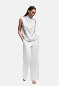 Witte mouwloze top met een cowl hals, gecombineerd met loszittende witte broeken. Gladde stof met een ontspannen pasvorm. Eenvoudig ontwerp, minimale details.