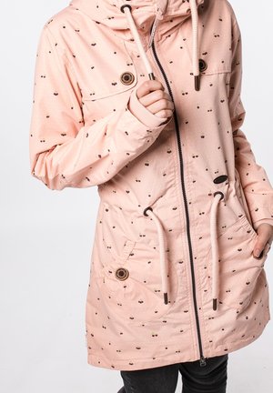 Veste à capuche rose clair avec petits motifs de cerises, fermeture éclair frontale, cordons de serrage, poches à boutons et poignets côtelés sur pantalon noir.