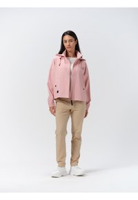 Helle rosa wasserdichte Jacke mit Kapuze, ausgestattet mit einem Frontreißverschluss, Kordeln und schwarzen Akzenten, kombiniert mit beigen Hosen und weißen Sneakern.