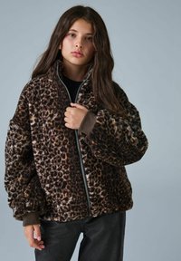 Braunes Leopardenjackett aus weichem, plüschigem Stoff. Hat einen hohen Kragen, einen durchgehenden Reißverschluss und dunkle Bündchen. Schwarze Hose sichtbar.