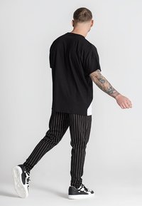 Černé oversized tričko vyrobené z bavlny, v kombinaci s černobílými pruhovanými kalhotami. Bílé mohutné tenisky s černými akcenty dotvářejí celkový vzhled.