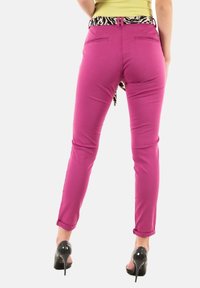 Slimované jasně růžové kalhoty s zadními kapsami a kontrastním páskem s černobílým vzorem, s ohrnutými nohavicemi a hladkou texturou.