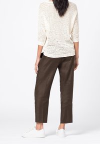Krémový pletený svetr s tříčtvrtečními rukávy, kombinovaný s hnědými volnými kalhotami a bílými teniskami. Viditelná textura pleteniny.