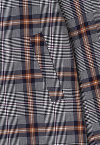 Tejido de mezcla de lana con un clásico patrón de jaquard y cuadros en gris, azul marino y naranja. Cuenta con un bolsillo lateral y un tejido texturizado.