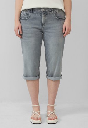 Graue Denim-Caprihosen mit umgeschlagenen Säumen, klassischem Fünf-Taschen-Design und leichter Used-Optik. Getragen mit weißen Riemchensandalen.