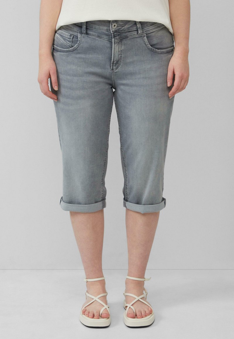 Grijze denim capri broek met opgerolde pijpen, voorzien van een klassieke vijf-pocket ontwerp en lichte slijtage. G gedragen met witte sandaaltjes met bandjes.