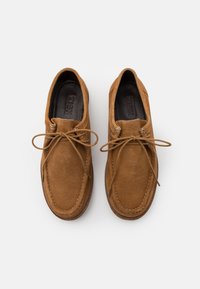Brązowe zamszowe buty z okrągłymi czubkami, haftowanymi detalami i sznurowaniami. Gładka tekstura z prostym, klasycznym wzorem.