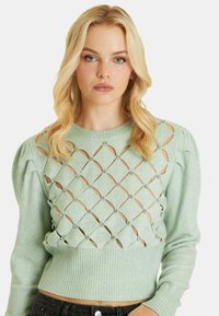 Maglione lavorato a maglia verde menta con maniche a sbuffo, caratterizzato da tagli a diamante e pietre decorative. Fondo a coste in vita.