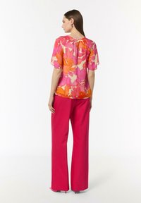 Kwiatowa bluzka w odcieniach różu i pomarańczy z krótkimi rękawami i marszczonym tyłem, zestawiona z różowymi spodniami o wysokim stanie.