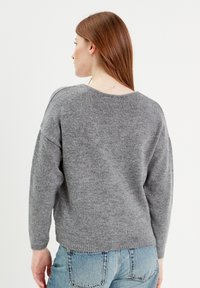 Maglione grigio lavorato a maglia con una vestibilità ampia, scollo rotondo e maniche lunghe. La texture è morbida, arricchita da polsini e orlo a costine.