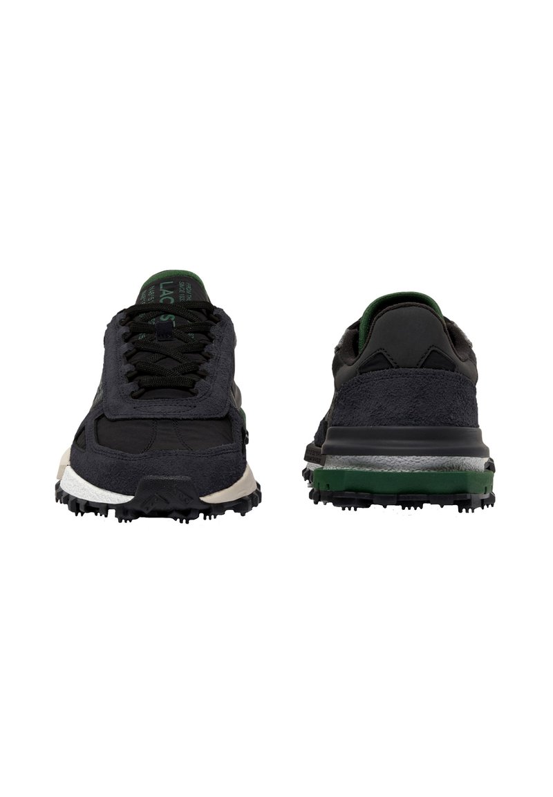 Zapatillas deportivas negras y verdes mostradas de frente y de espaldas, con suelas texturizadas y diseño con cordones, sobre un fondo blanco.