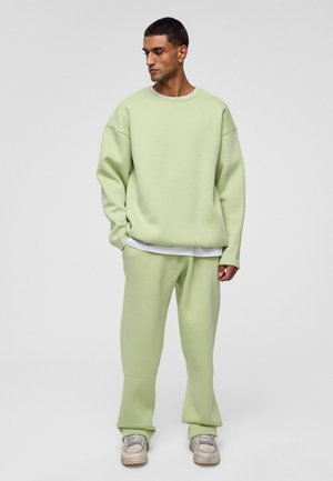 Lichtgroene oversized sweatshirt en bijpassende broek gemaakt van een zachte, gladde stof. Het sweatshirt heeft een ronde halslijn en overeind staande schouders.