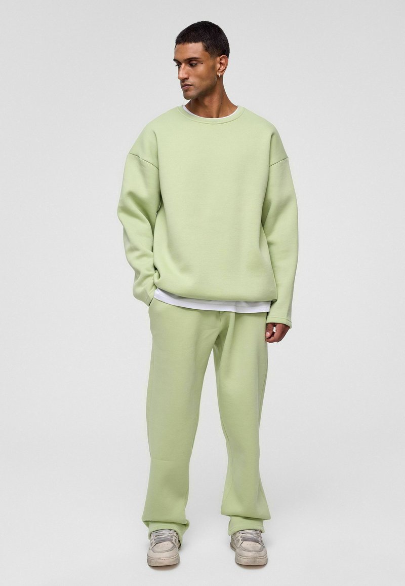 Lichtgroene oversized sweatshirt en bijpassende broek gemaakt van een zachte, gladde stof. Het sweatshirt heeft een ronde halslijn en overeind staande schouders.