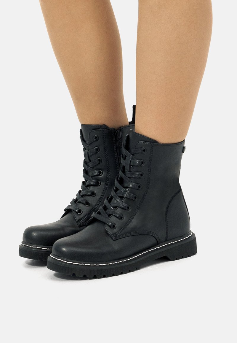 Botas de combate de cuero negro con cordones en la parte delantera, cremallera lateral, suela de goma gruesa y detalle de costura blanca a lo largo del borde.