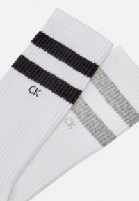Calcetines blancos con canalé y rayas negras y grises en la parte superior. Presentan un pequeño logo de CK cerca del tobillo en cada par.