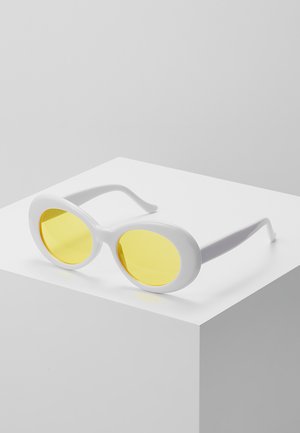 Gafas de sol blancas con lentes ovalados. Lentes de tono amarillo y montura lisa y brillante. Diseño sencillo con brazos delgados y curvados.