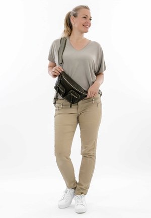 Černá crossbody kabelka z umělé kůže se dvěma zipovými předními kapsami. Stylizováno s volným šedým topem a hnědými kalhotami. Bílé tenisky doplňují vzhled.