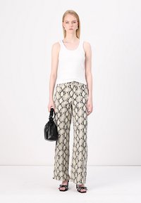Top sin mangas blanco, pantalones de pierna ancha con estampado de serpiente en beige y negro, bolso negro, sandalias de tacón abierto con lunares negros y blancos.