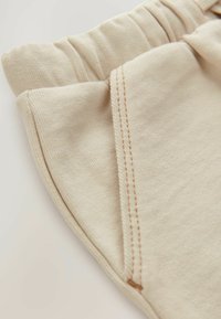 Pantalon en coton beige au toucher doux, avec une taille élastique et des détails de couture contrastés le long des bords et des poches.