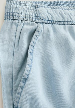 Șorturi din denim de un albastru deschis, cu un band desg elastic, buzunare laterale și o textură moale; prezintă cusături distincte de-a lungul îmbinărilor.