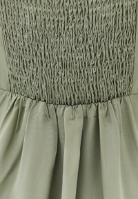 Zielona sukienka z marszczonym gorsetem i teksturowanymi fałdami, wykonana z lekkiego materiału, tworząca zwiewną sylwetkę.