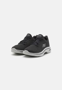 Scarpe da ginnastica nere in rete con una finitura testurizzata, caratterizzate da accenti grigi, design con lacci e una suola bianca ammortizzata.