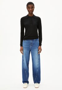 Zwarte polo met lange mouwen, kraag en knopen, gecombineerd met wijdvallende lichtblauwe jeans met een vervaagde afwerking en witte sneakers.