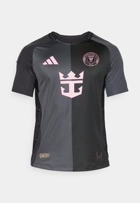 Svart tröja med rosa detaljer, en kronlogotyp och Adidas-logotypen. Tillverkad av lättviktig tyg, har den rundad halsringning och korta ärmar.