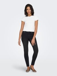 Bijeli crop top rebrastog uzorka s zaobljenim kratkim rukavima, uparen s crnim uskim trapericama i smeđim balerinkama. Odjevna kombinacija ima uski kroj.