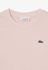 Camiseta de corte oversize en rosa claro, hecha de algodón suave, con un pequeño logotipo de cocodrilo bordado en la zona izquierda del pecho.