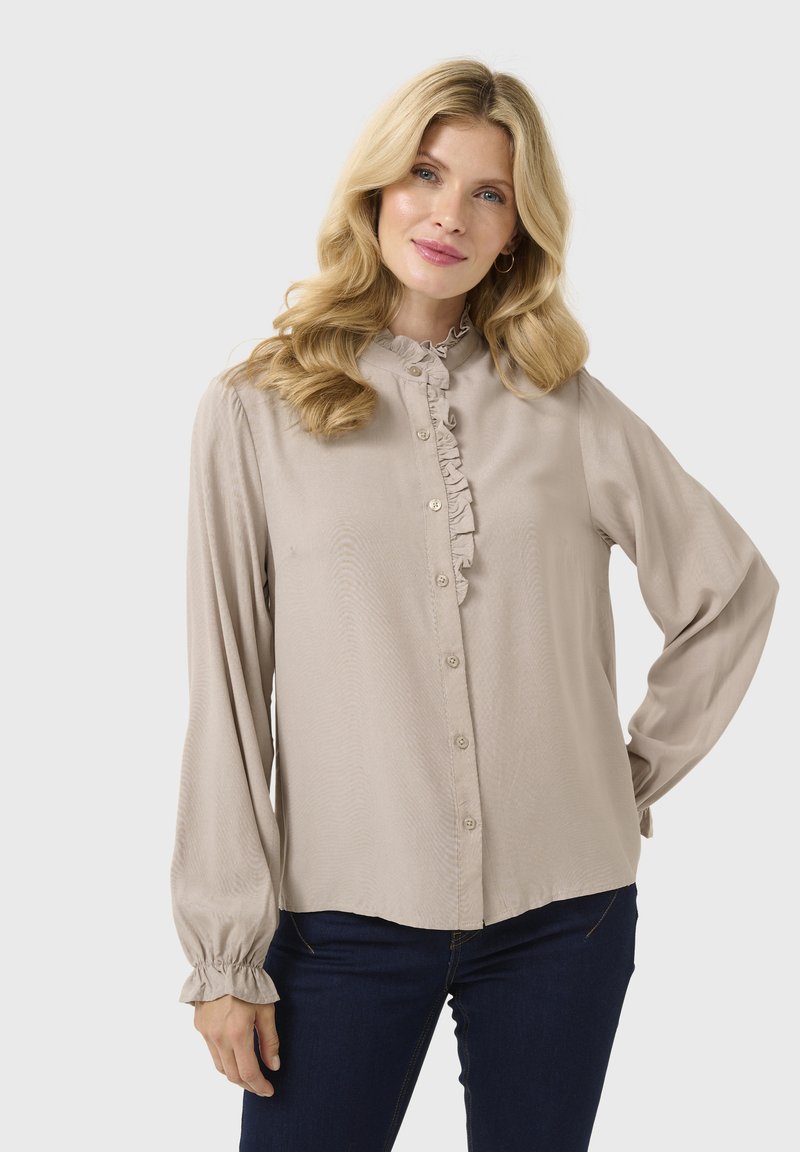 Blusa beige chiara con colletto arricciato e apertura con bottoni, dotata di maniche lunghe con polsini elastici e una morbida e liscia texture.